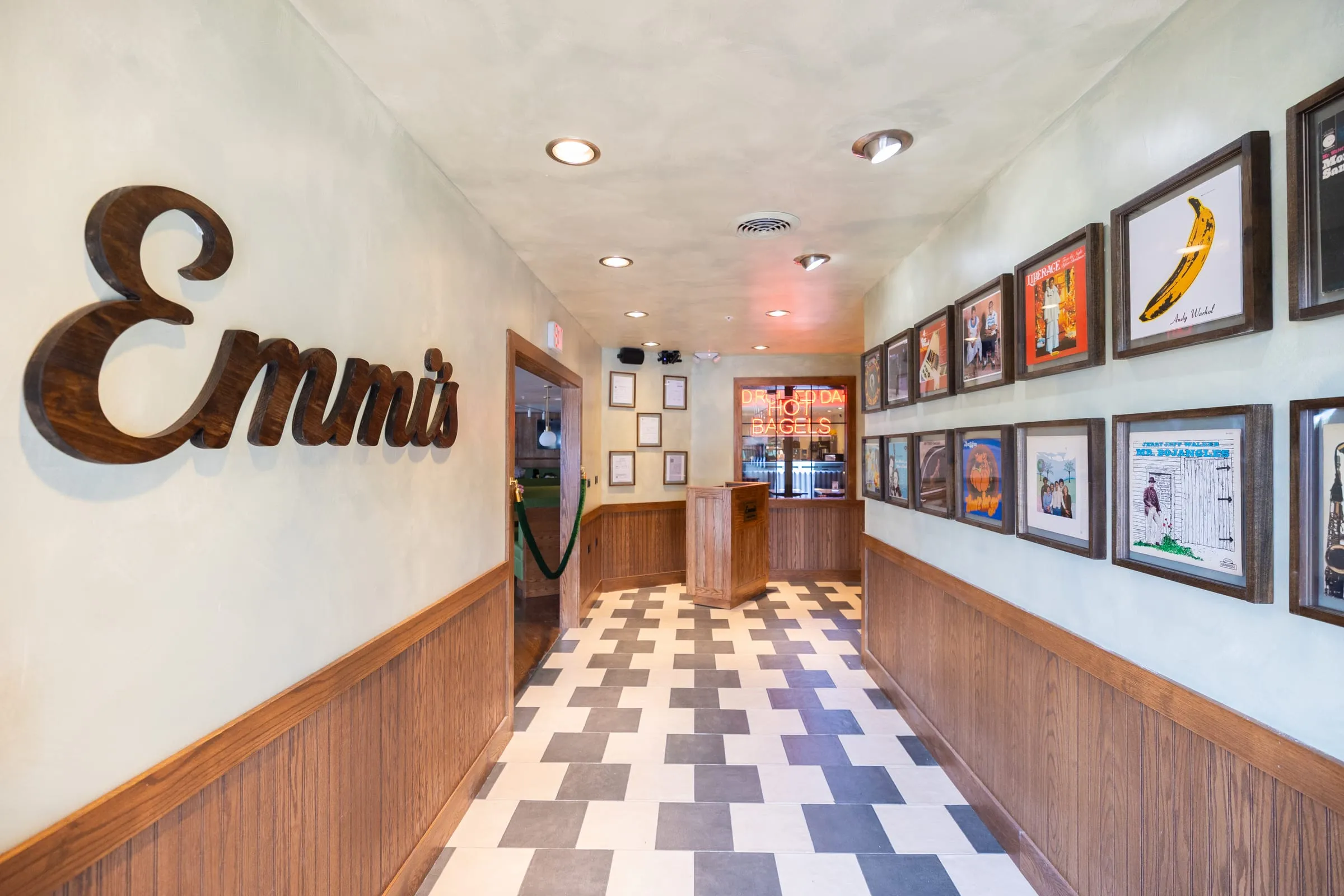 Emmi’s entryway with a wooden script sign, checkered tile floor, and framed record covers leading to the host stand.