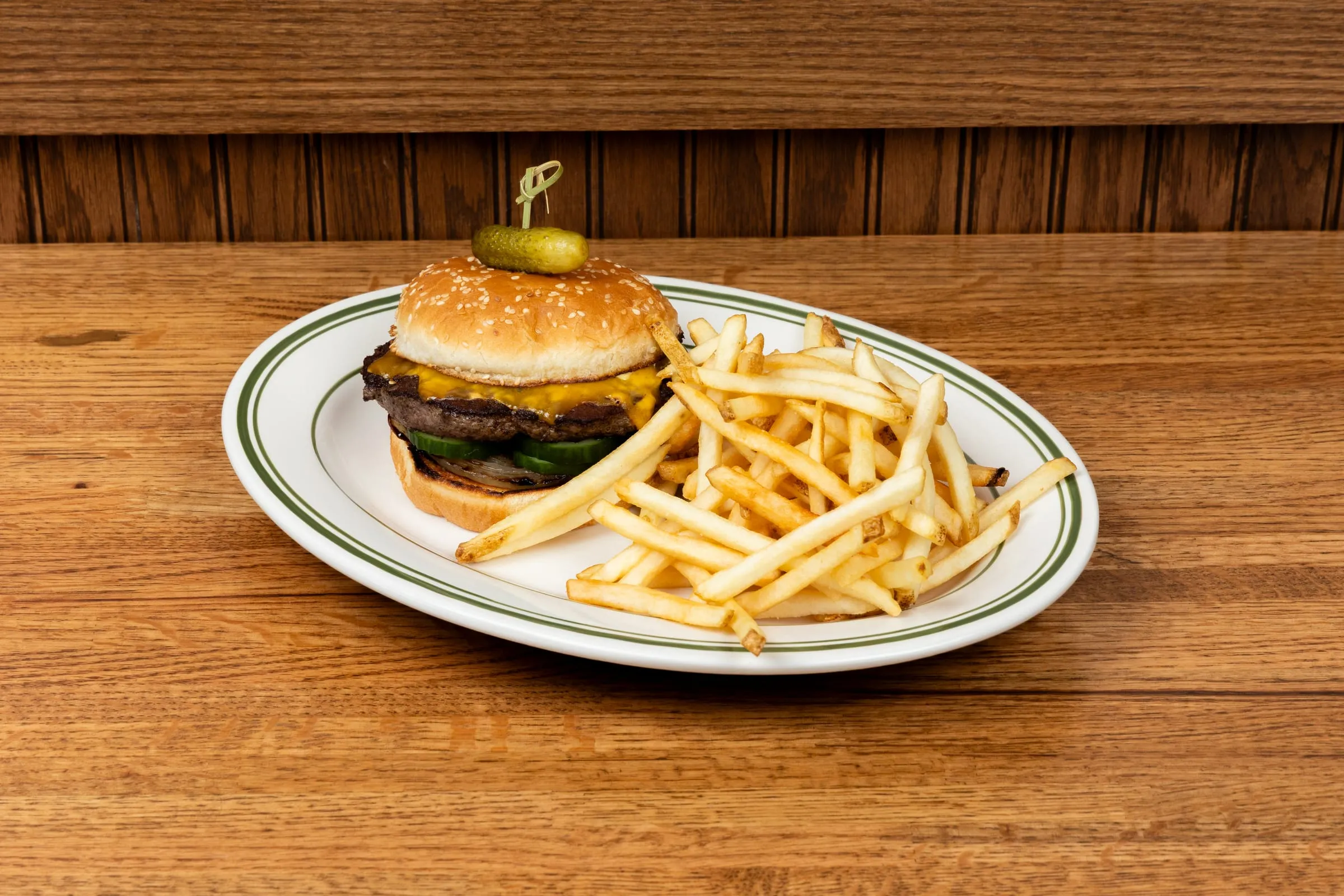 Emmi's Famous Burger — a cheeseburger on a sesame bun topped with a pickle, served with shoestring fries on a green-striped plate.