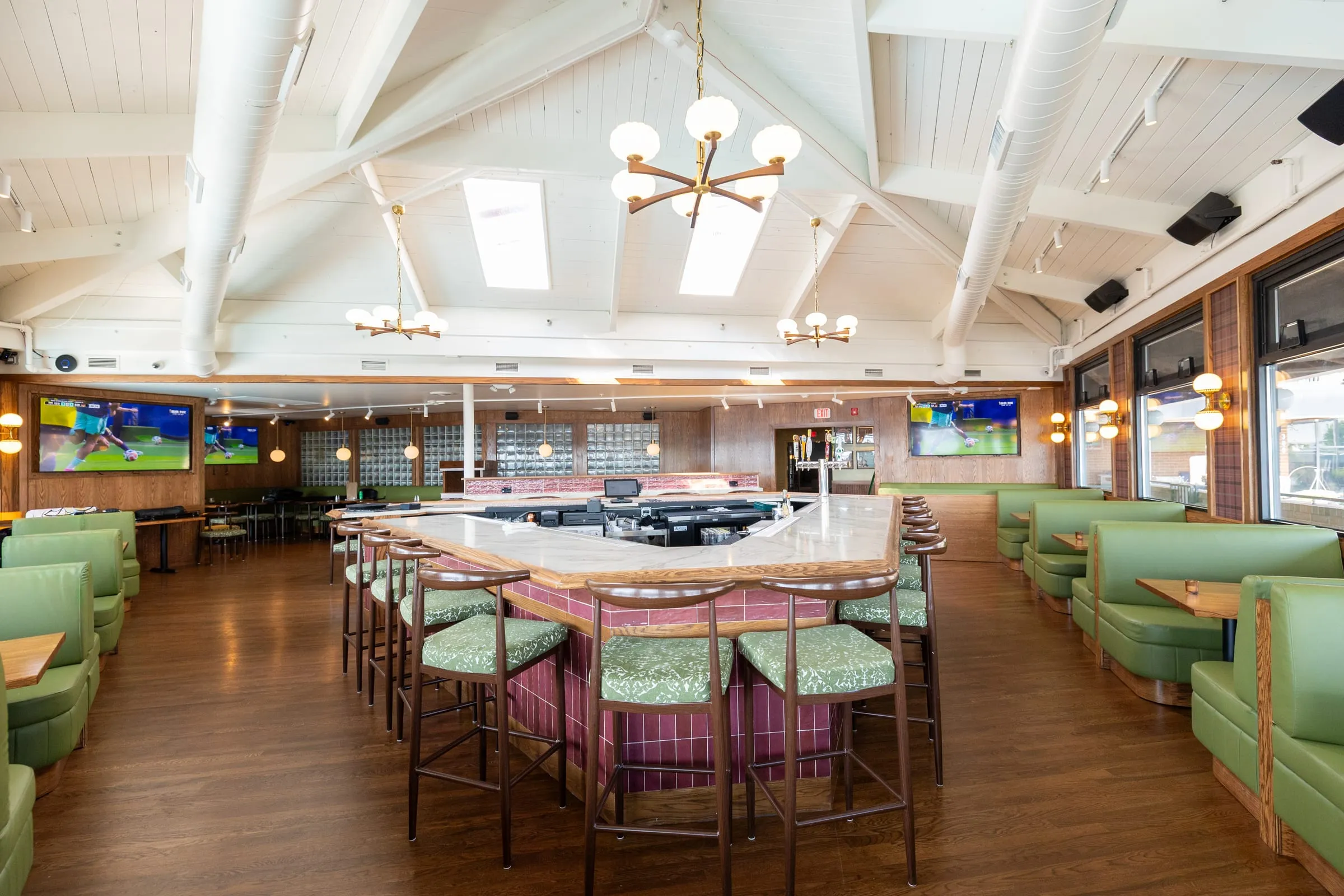 Emmi's main dining room, with green booths, a marble-topped bar, and mid-century chandeliers under a vaulted white ceiling.