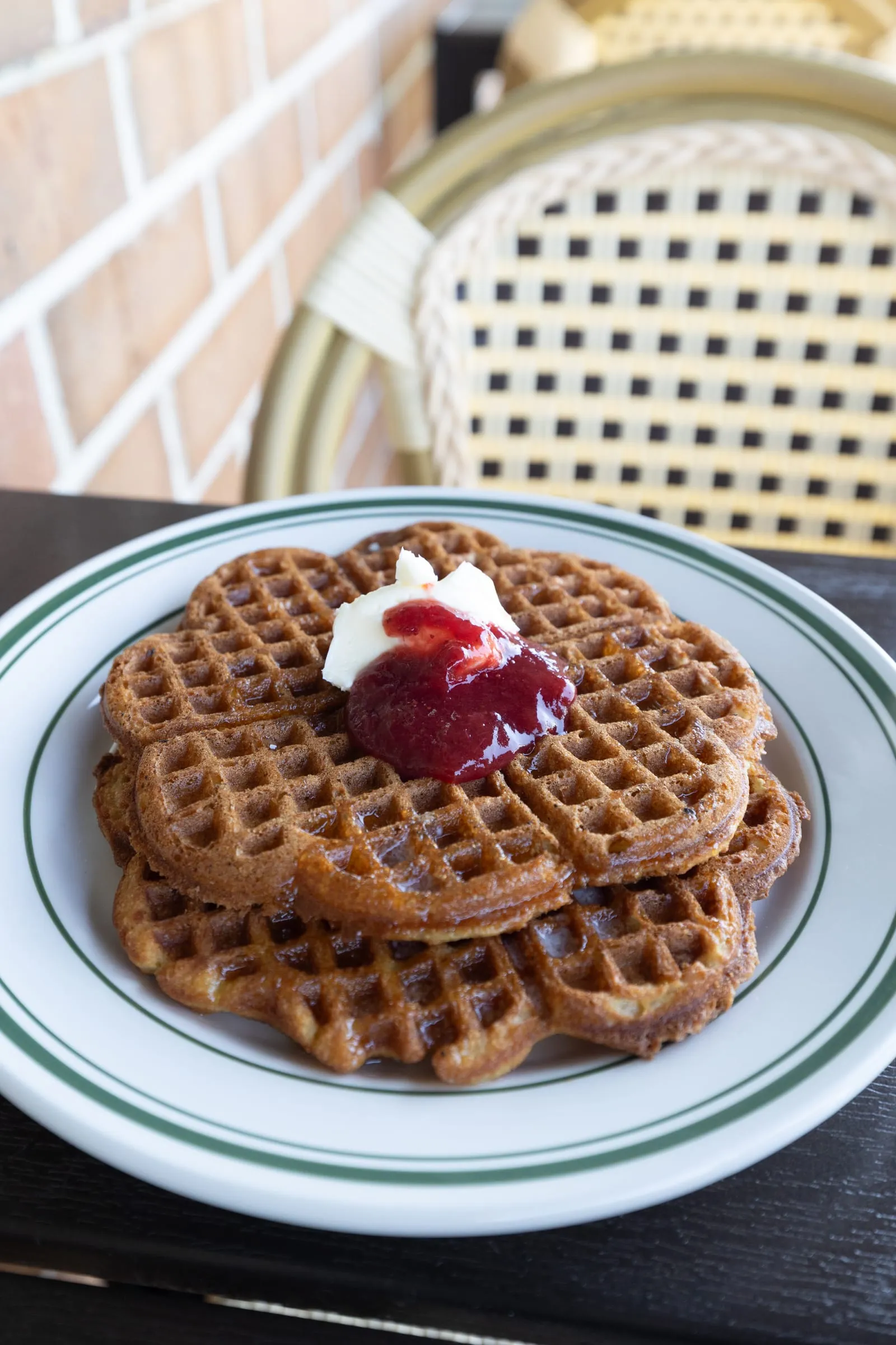 Norwegian waffles topped with butter and lingonberry jam on a green-striped plate.