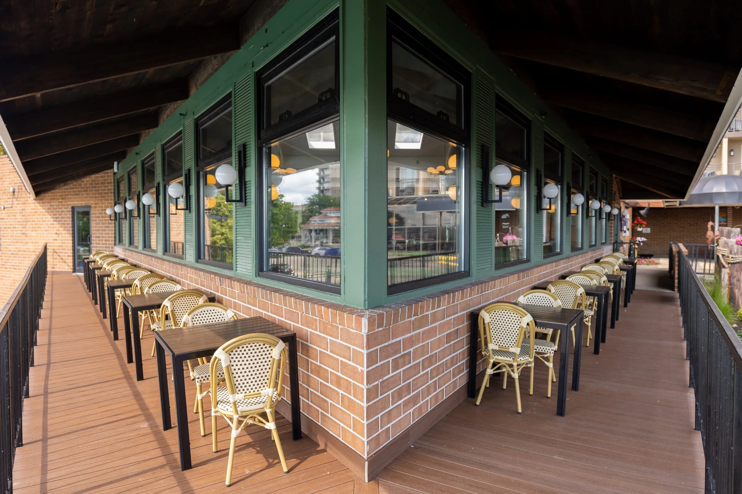 Tables and woven café chairs on Emmi's covered outdoor deck, wrapping around the green-trimmed corner of the restaurant.