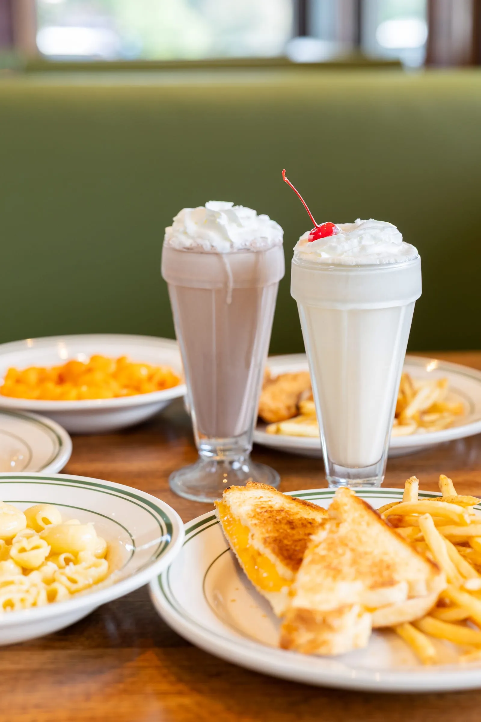 Chocolate and vanilla milkshakes with whipped cream and a cherry, alongside kids plates of grilled cheese, fries, and macaroni.