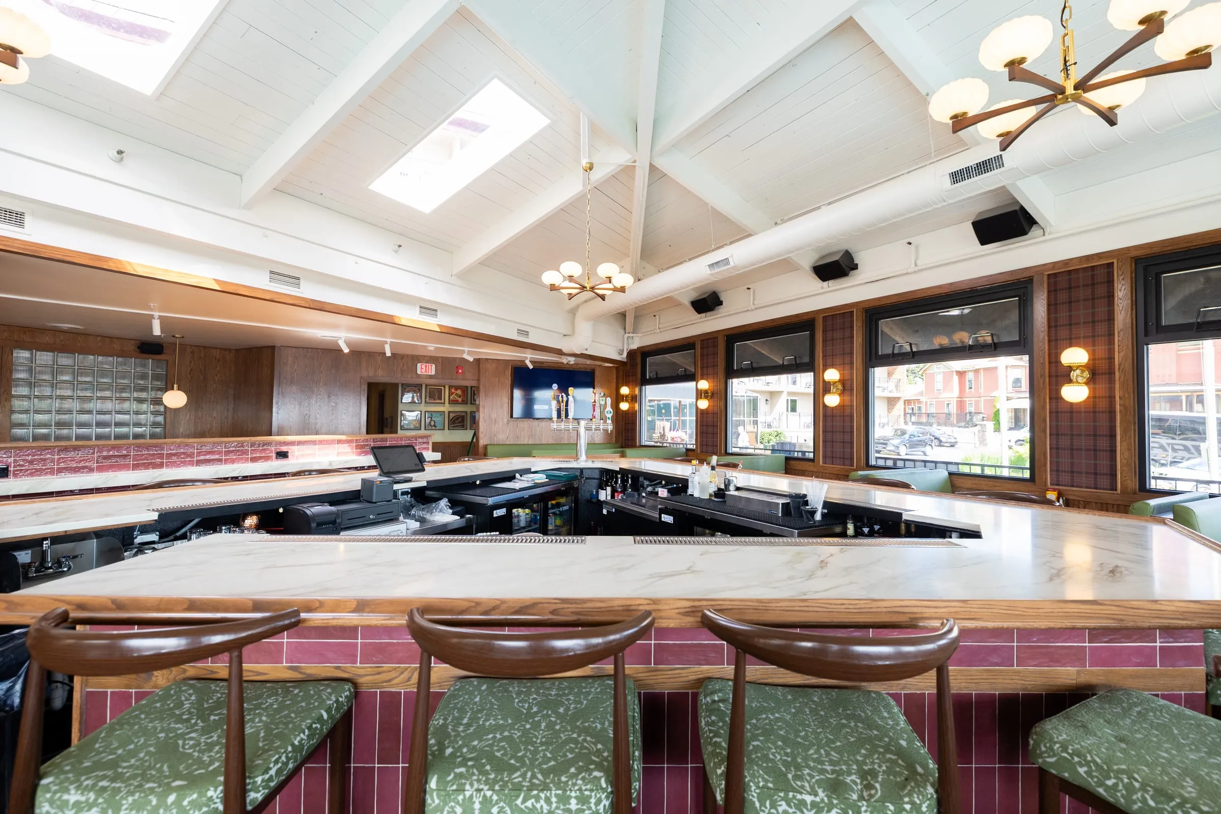 Emmi's marble-topped bar with beer taps and green upholstered bar stools, under skylights and brass chandeliers.