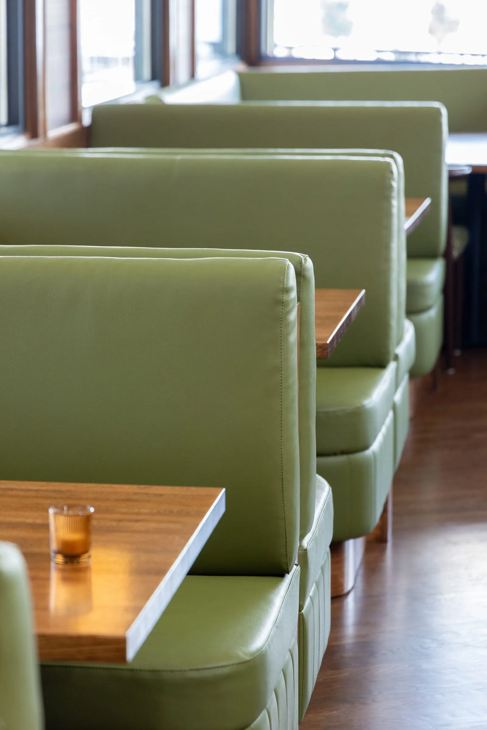 A row of green leather booths with warm wood tables beside the windows at Emmi's, each set with a small amber candle.